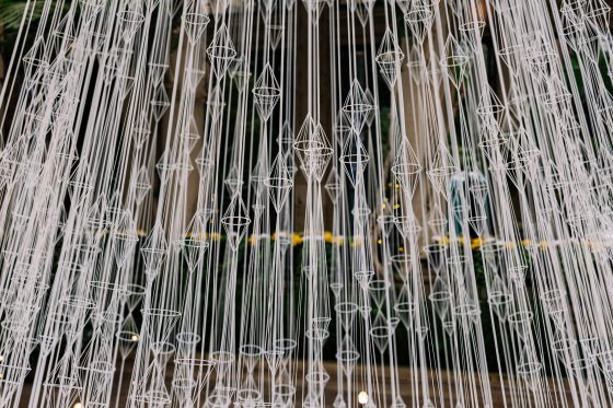 A close up of hundred of white strings crafted into geometric patterns, put together in the shape of a tree.